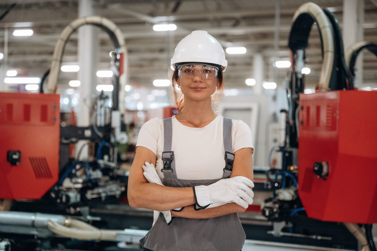 Professional woman in safety equipment standing in industrial warehouse with machinery